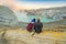 Young tourist man and woman sit at the edge of the crater of the Ijen volcano or Kawah Ijen on the Indonesian language