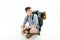 Young tourist is sitting with backpack on white background. traveler is preparing for hike