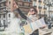 Young tourist is standing on street of European city near fountain,holding map and pointing at something with her finger