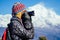 A young tourist woman with a hiking backpack and a knitted hat photographing landscapes in the Himalaya Mountains