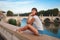 Young tourist woman sitting on the ancient embankment Tiber in Roma at sunset. Near of bridge and castle of Angels. Saint Angelo