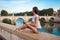 Young tourist woman sitting on the ancient embankment Tiber in Roma at sunset. Near of bridge and castle of Angels. Saint Angelo