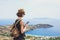 Young tourist woman using smartphone over beautiful landscape with sea in Greece. Traveler girl with backpack and mobile phone.