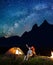 Young tourists man and woman looking at the shines starry sky at night. Happy couple sitting near tent and campfire