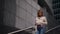 Young townswoman in city, walking in modern district in daytime, moving down on stairs