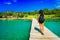 Young travel girl backpacker walks with backpack along a scenery wooden bridge to a tropical paradise island