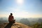 young traveler with backpack sit on the mountain peak rock observing locality