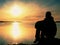 Young traveler man at sunset. Tourist sitting on the cliff above lake