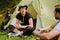 Young travelers resting in tents while hiking in green forest