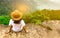 Young traveling woman wearing hat and sitting on the top of the mountain cliff with relaxing mood and watching beautiful view