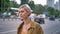 Young trendy woman with short pink hair waiting for taxi or bus, standing on urban street near road