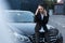 Young troubled businesswoman sitting on hood of passenger car and talking