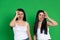 Young twin girls gesturing okay make faces with tongues out on a green background with space