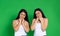 Young twin girls pose cute against green background and look tenderly into the camera