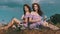 Young Twin Womens Sit Back to Back Together in Identical Dresses on the Grass