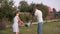 Young Two Parent Family In The Garden With Their Young Son. They Are Holding Hands And Swinging The Little Boy.