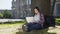 Young university student using laptop, sitting under tree, smiling, socializing