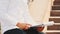 A young unrecognisable businessman with clipboard and pen, wearing white shirt, is outside in city, sitting on bench