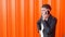 Young unshaven caucasian guy in a black jacket emotionally talking on the phone and is angry at the orange background