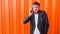 Young unshaven caucasian man in a black jacket talking on the phone on an orange background, slow-mo, fashionable