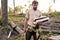 Young unshaven guy in T-shirt holds firewood in hands at summer in forest.