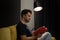 Young unshaven handsome guy reads book sitting on yellow sofa under spot lamp