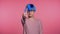 Young unusual woman with blue hair making disapproving with no finger sign, negation gesture over pink studio background