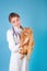 Young veterinarian woman holding red british cat on blue background