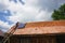 Young volunteer man up on a ladder, installing a photovoltaic solar panel on the roof of an old house