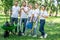 young volunteers posing in park with watering can shovel rake and wheelbarrow