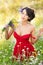 Young voluptuous brunette holding a wild flowers bouquet in a sunny day. Portrait of beautiful woman with low-cut red dress posing