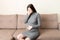 Young vomiting woman sitting on sofa and suffering with nausea. Pregnancy expectation concept, copy space