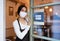 Young waitress with face mask by entrance door in cafe, reopening concept.