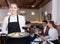 Young waitress with serving tray meeting restaurant guests