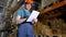 A young warehouse worker walks and takes note on paper.