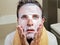 Young weird and funny man at home trying using beauty paper facial mask cleansing learning anti aging treatment in surprised  face