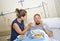 Young wife trying to feed his reluctant husband lying in bed at hospital room ill after suffering accident