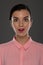 A young woman of 30-35 years old in a pink blouse on a gray background, restrained emotions. Maybe she works in an office