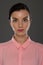 A young woman of 30-35 years old in a pink blouse on a gray background, restrained emotions. Maybe she works in an office