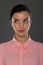 A young woman of 30-35 years old in a pink blouse on a gray background, restrained emotions. Maybe she works in an office