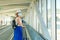 Young woman 40s in protective face mask with a suitcase riding escalator in airport terminal. Safety travelling alone