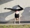 Young woman acrobat on handstand performs twine against the wall outdoors