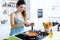 Young woman adding pepper and mixing food in frying pan.