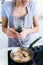 Young woman adding pepper to chicken into the pan