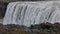 A young woman admires a powerful raging waterfall that falls heavily along a rocky edge. A crystal clear stream of glacier water f