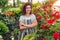 Young woman admiring her summer garden. Gardener in apron and hat looking at flowers. Hobby