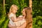 Young woman affectionately looks at her little daughter, which she holds in her arms, against the background of nature