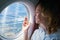 Young woman in the aircraft cabin looks through the porthole at the terrain below