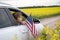 Young woman with an American flag looks out of the car window