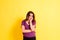 Young woman with anguished and uneasy expression  isolated on yellow studio background